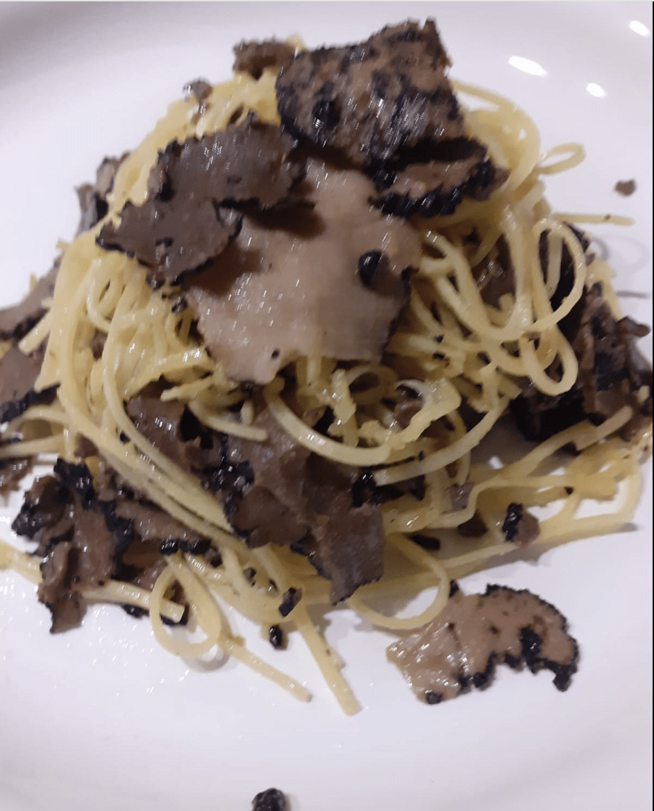 Taglierini affumicati con petali di tartufo nero estivo serviti su piatto bianco.